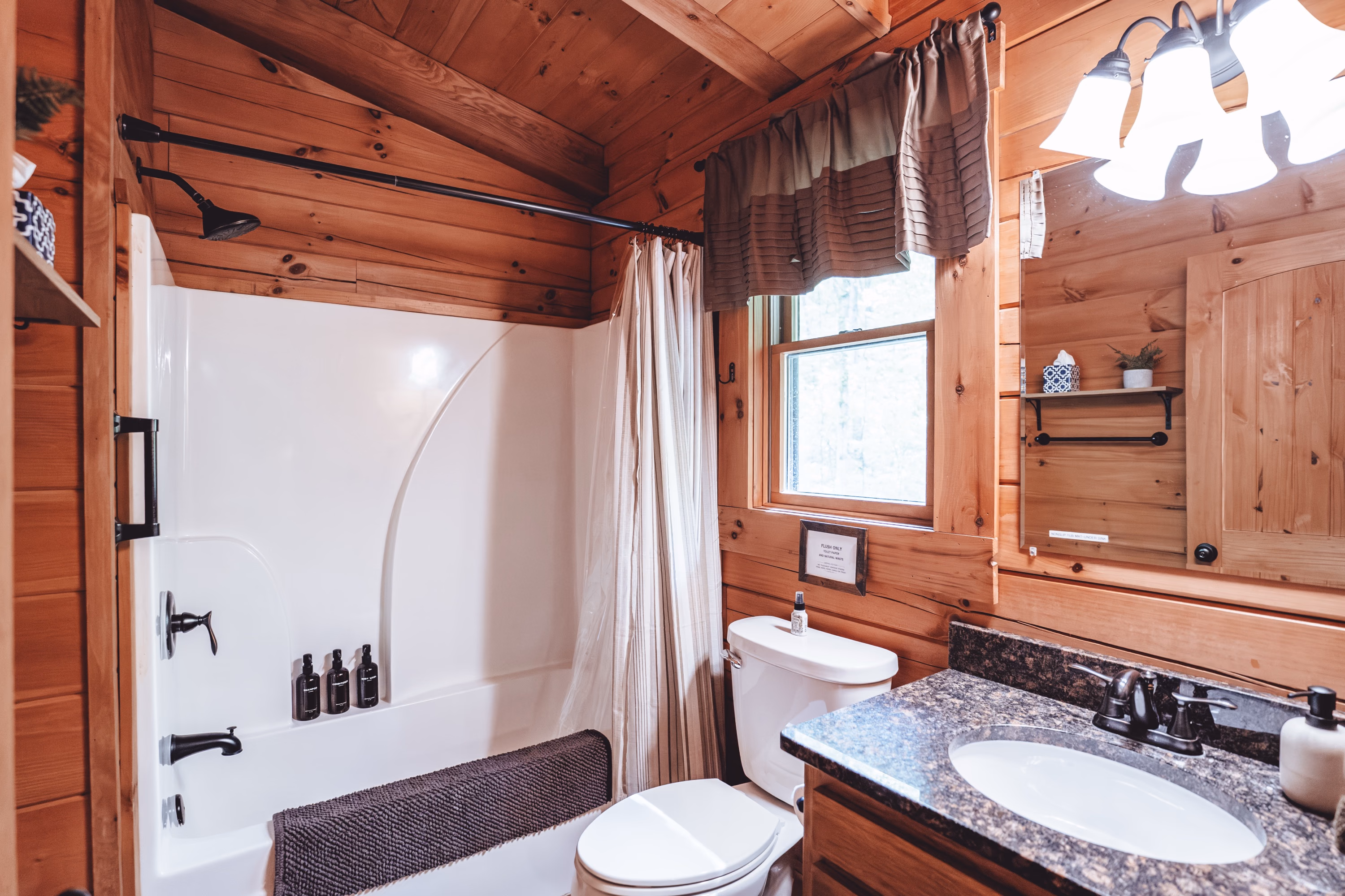 A bathroom with a tub and shower, granite vanity, and a window to the trees